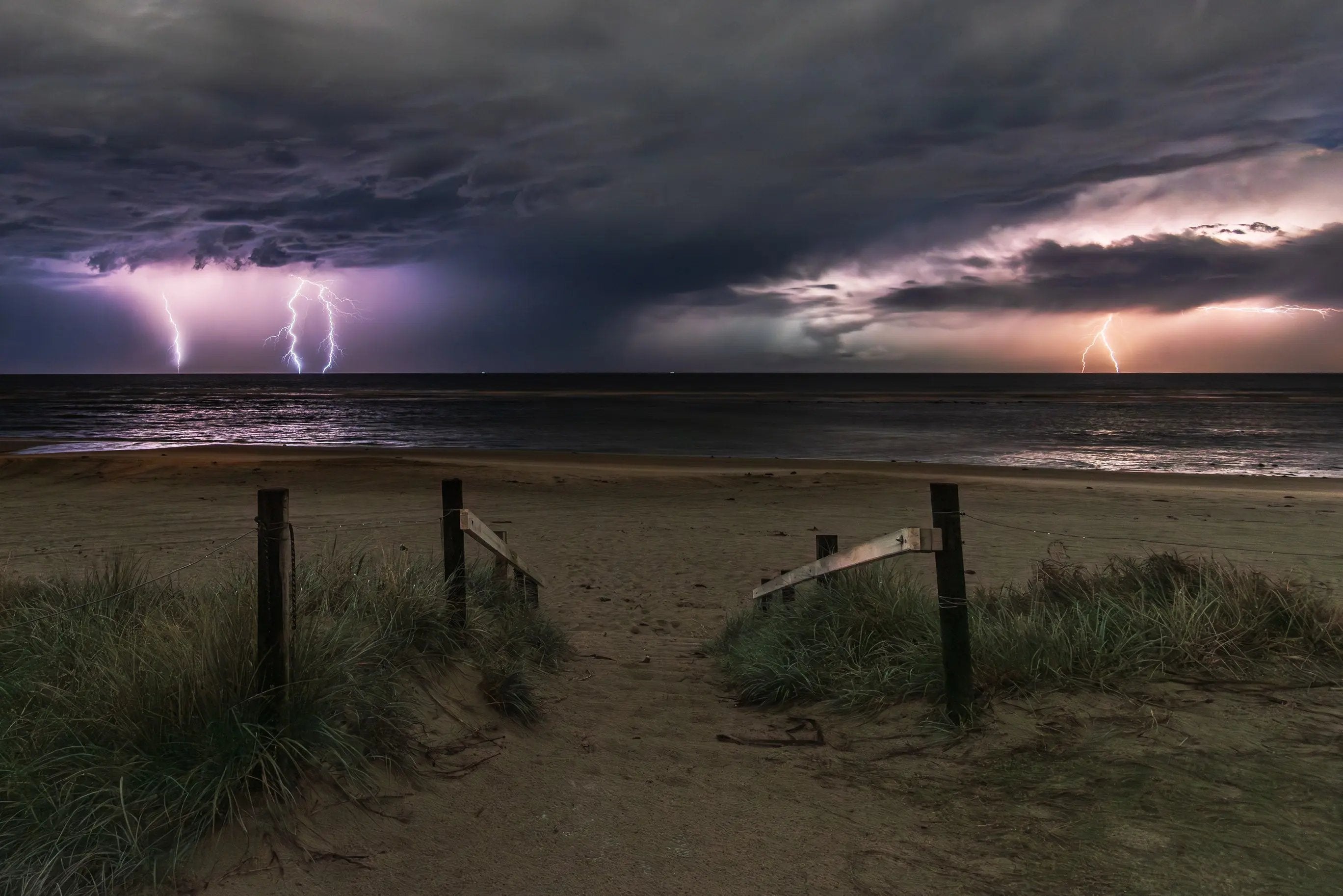 Beach scene with lightning strikes over the ocean under a dark sky.