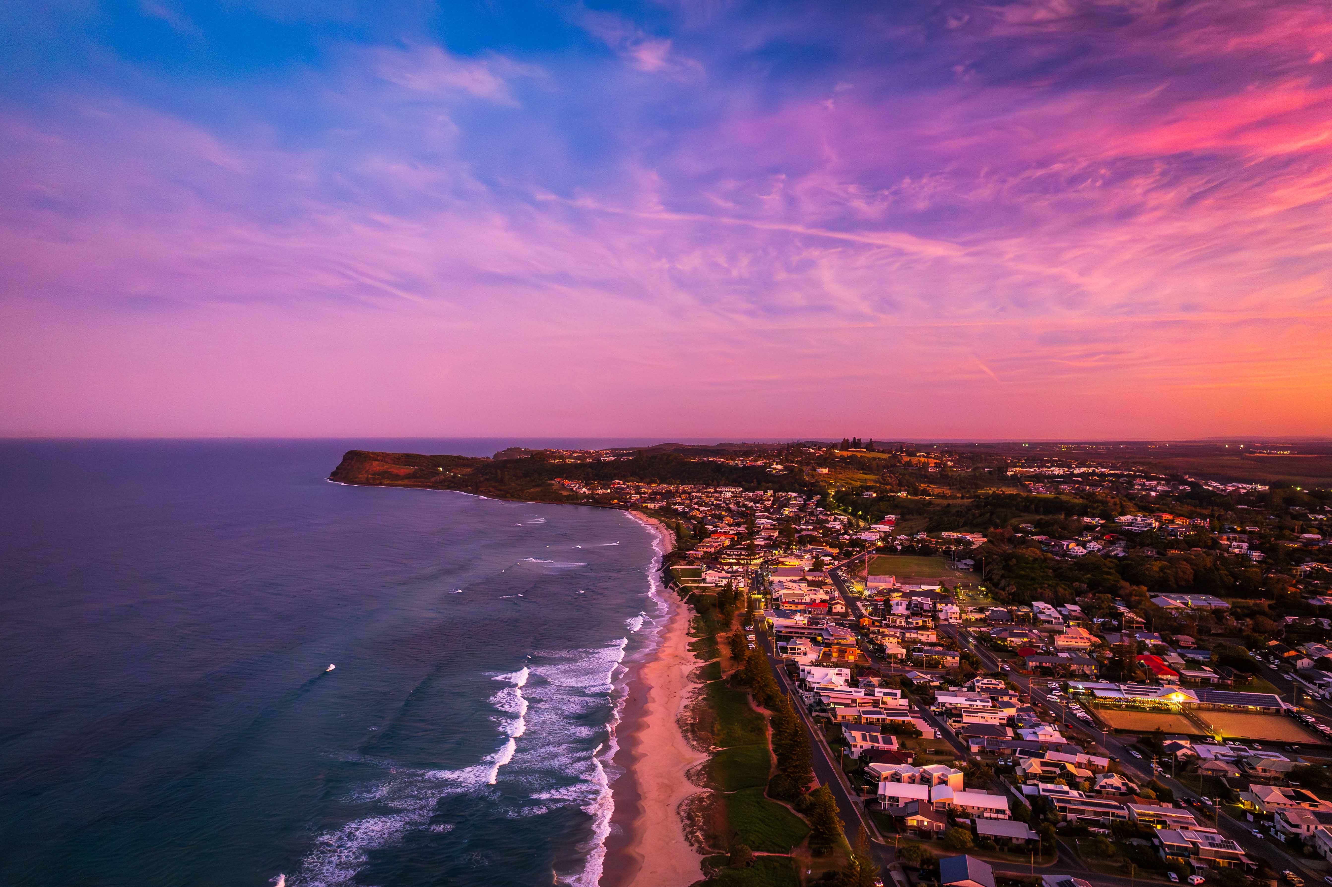 Aerial view of a coastal town at sunset with vibrant sky and ocean.