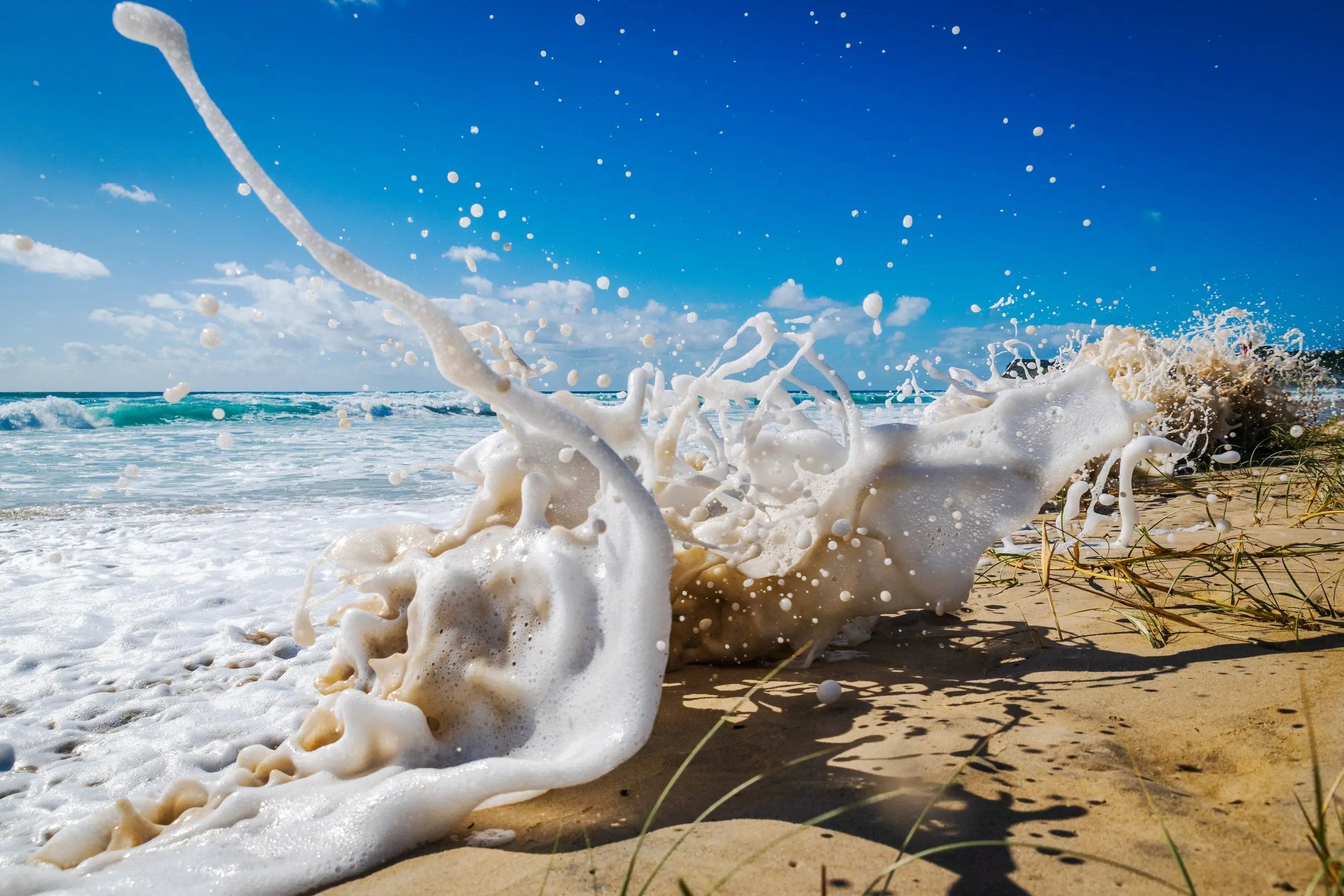 Foamy wave crashing onto a sandy beach with clear blue sky.