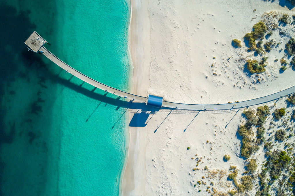 A photograph featuring a bridge extending over a body of water, with a sandy beach and vegetation in the background.