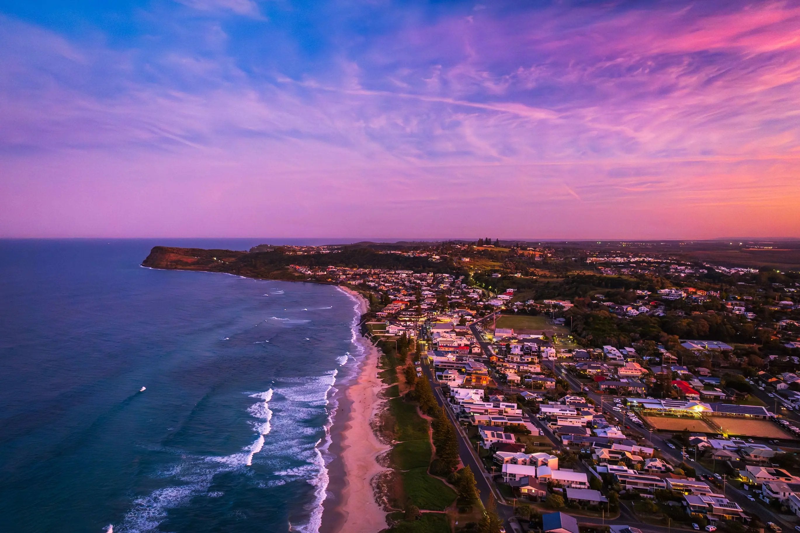 Aerial view of a coastal town at sunset with vibrant sky and ocean.