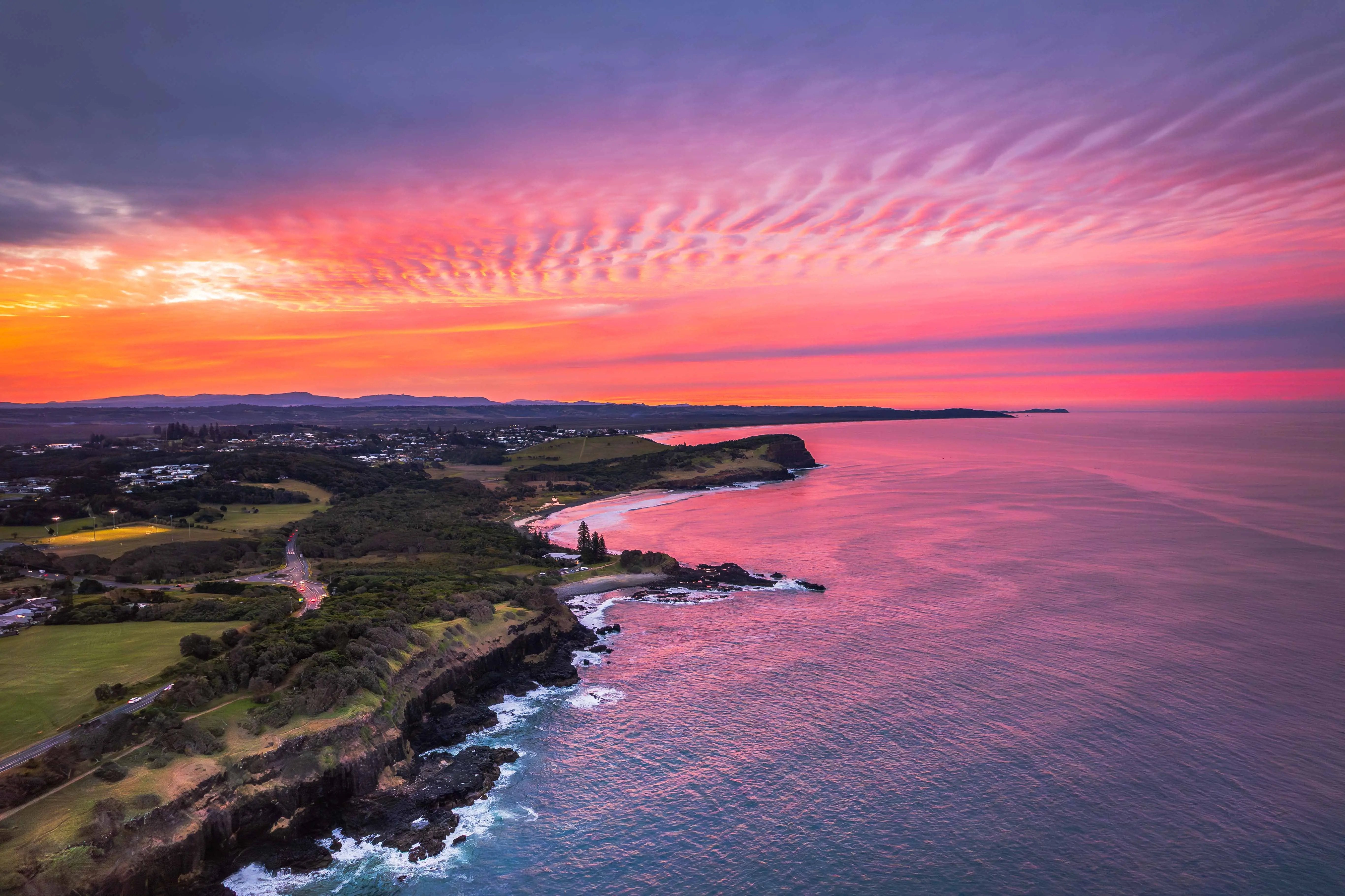 Sunset over a coastal landscape with pink and orange hues in the sky.
