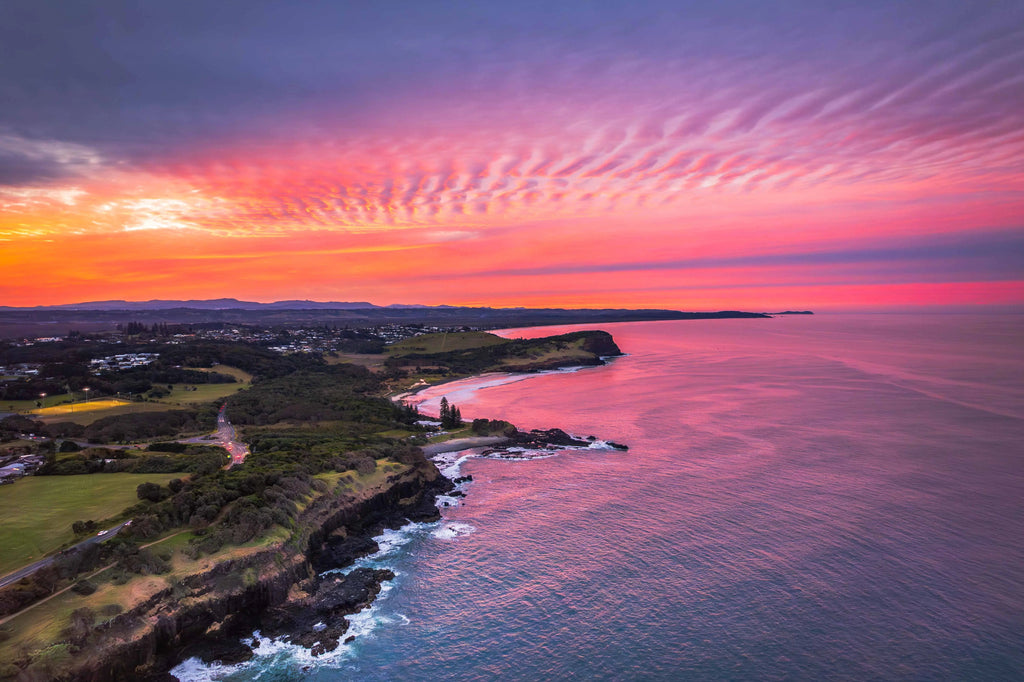 Sunset over a coastal landscape with pink and orange hues in the sky.
