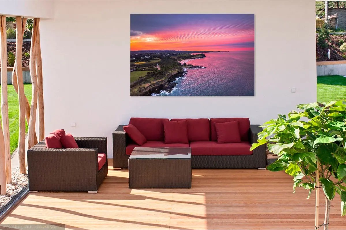 Outdoor furniture set with red cushions and a large wall art of a sunset over water.